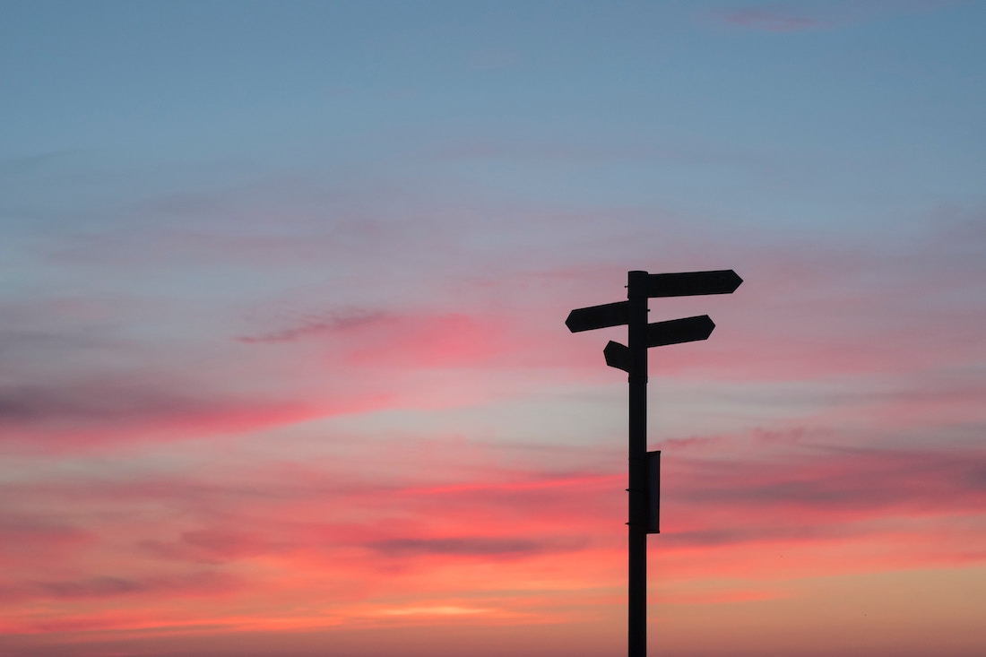 Photo of a sunset with a pole and direction signs.